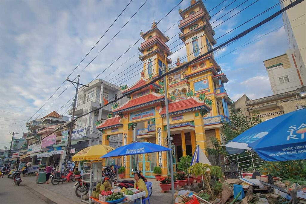 Colorful exterior of Cao Dai Temple in Phu Quoc surrounded by local shops scooters and street vendors