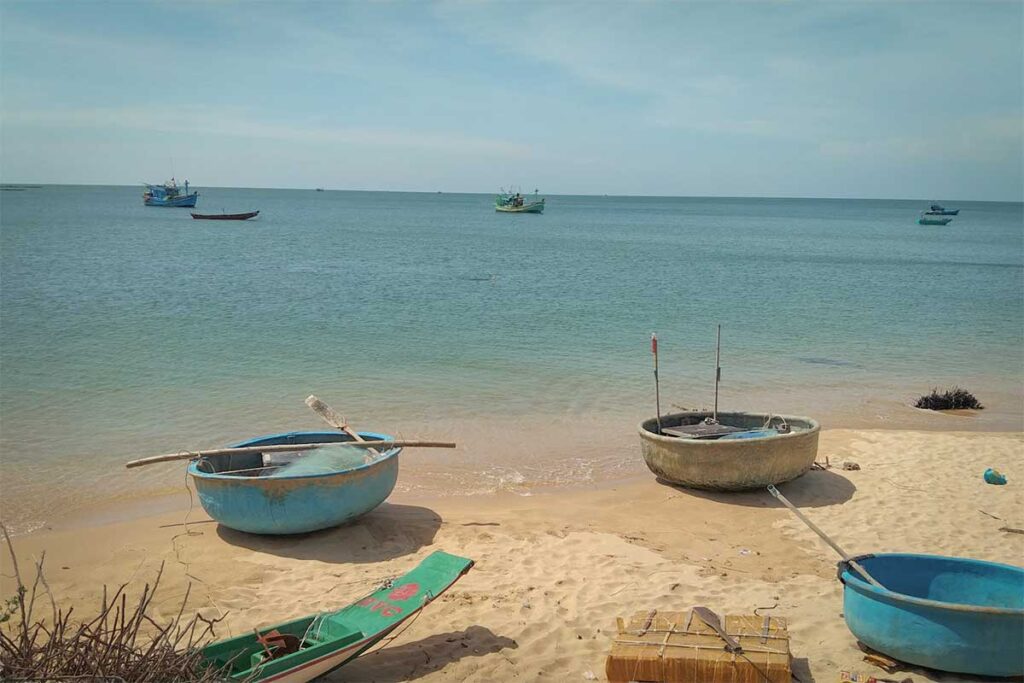 Round basket boats on the sandy beach in Ham Ninh fishing village Phu Quoc with fishing boats offshore