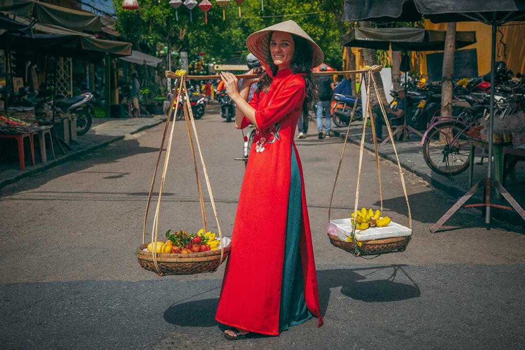 Traveler holding a traditional Vietnamese fruit carrying pole on a street, a common setup used for photos that can sometimes lead to unexpected charges