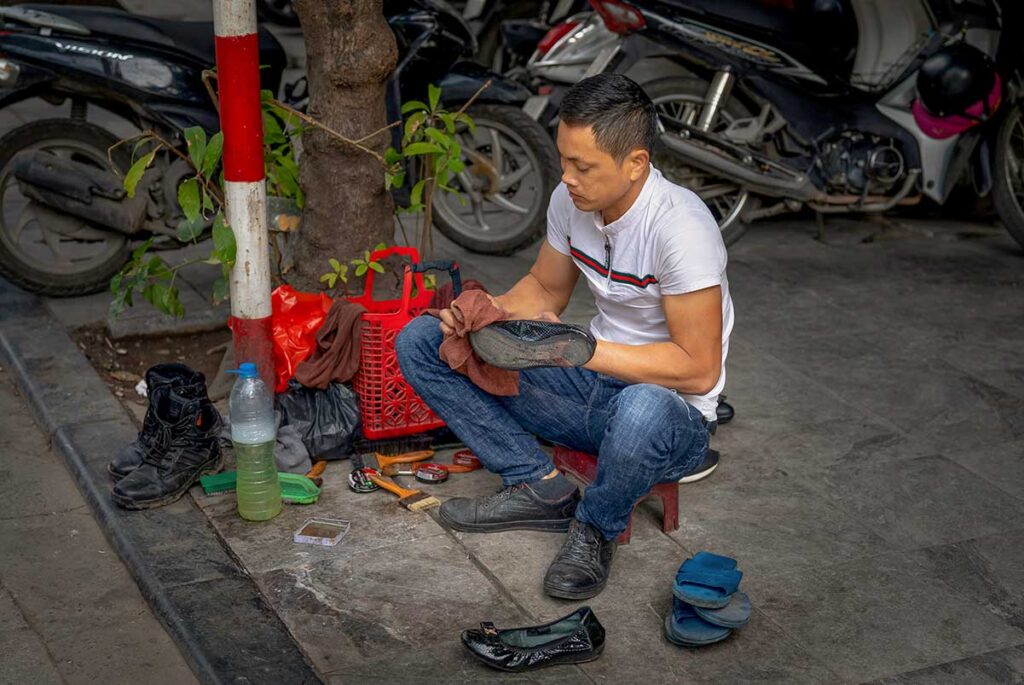 Shoeshiner cleaning shoes on a sidewalk in Vietnam, a common street service that sometimes starts without clear agreement