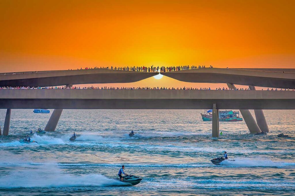 Kiss Bridge Phu Quoc at sunset with crowds on the bridge and jet skis racing on the sea during the evening show