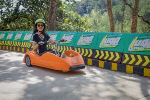 Person riding a downhill luge cart on the Mario Kart Dalat track, wearing a helmet and driving through a curved section of the course