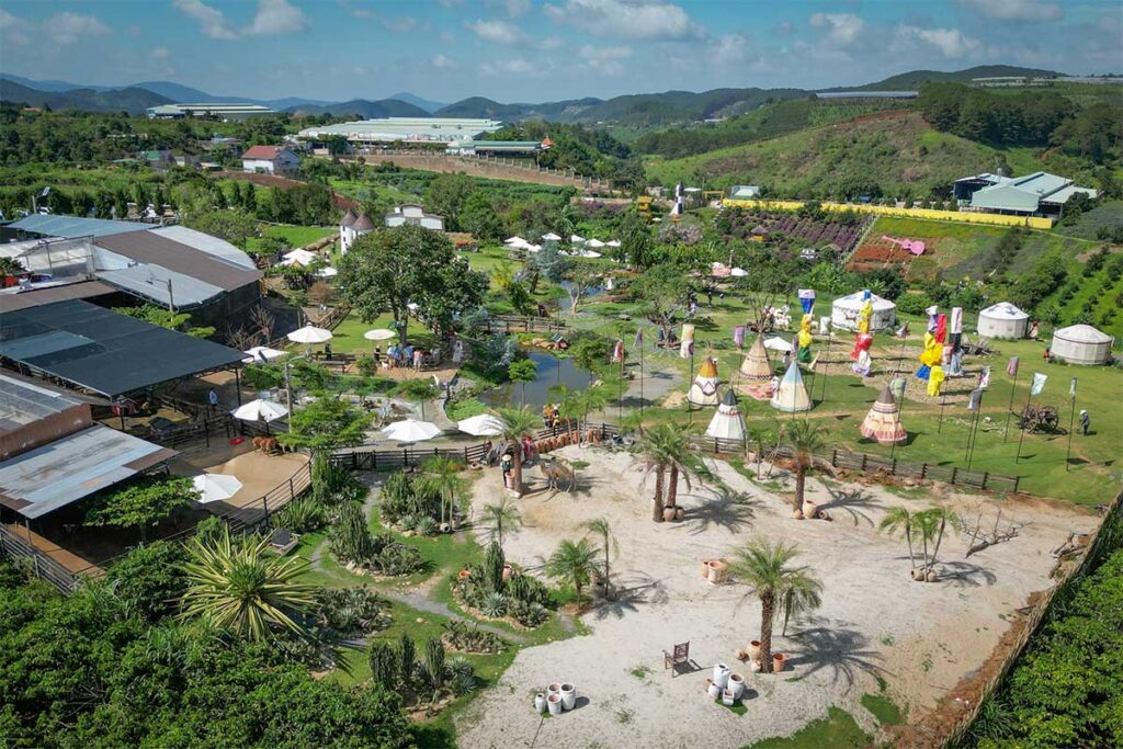 Overview of Mongo Land Dalat showing landscaped park areas, tents, gardens, and surrounding hills