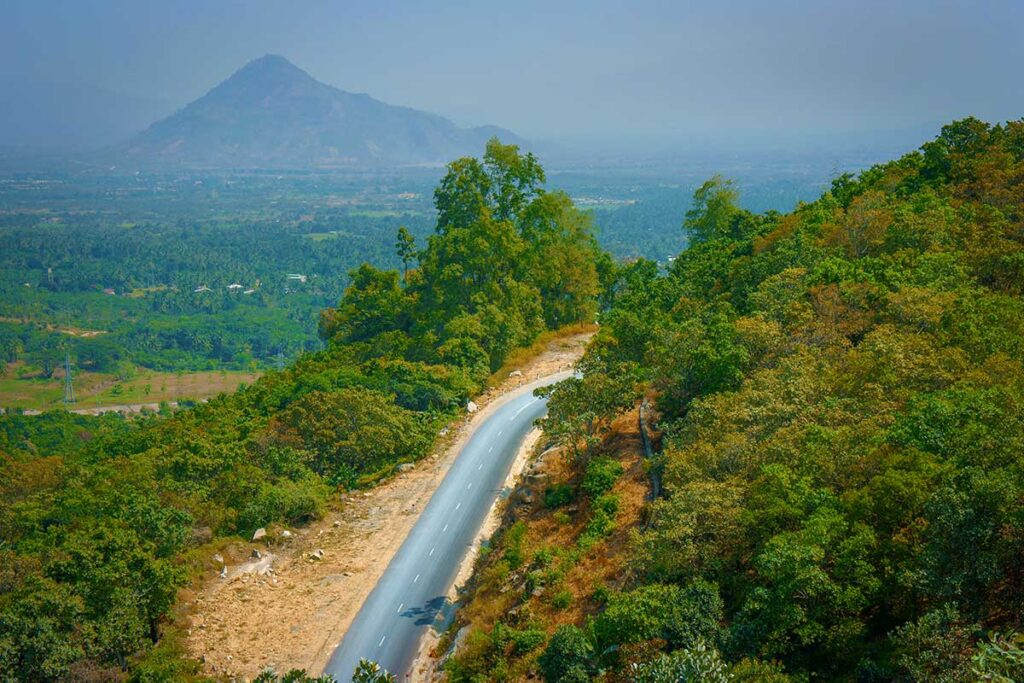 Mountain road of Ngoan Muc Pass cutting through forested hills with a view toward the dry landscape of the coastal plains below