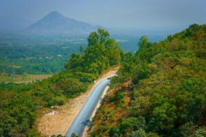 Mountain road of Ngoan Muc Pass cutting through forested hills with a view toward the dry landscape of the coastal plains below