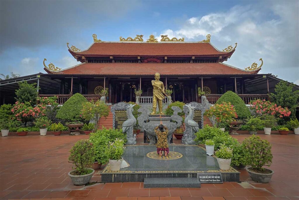 Visitor praying at Nguyen Trung Truc Temple in Phu Quoc in front of golden hero statue and main hall
