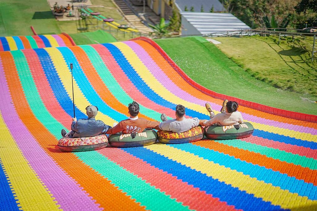 Rainbow slide at Dapa Hill Dalat with visitors riding down the slope on inflatable tubes surrounded by trees