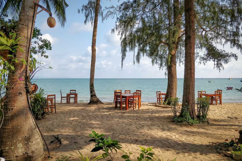 Beachfront restaurant tables on the sand at Vung Bau Beach Phu Quoc under shady trees facing the sea