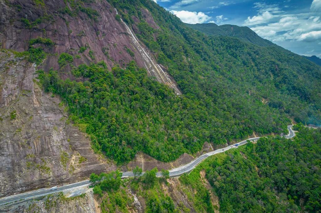 Mountain road of Khanh Le Pass winding along steep cliffs between Da Lat and Nha Trang, with dense forest and sharp curves visible along the route
