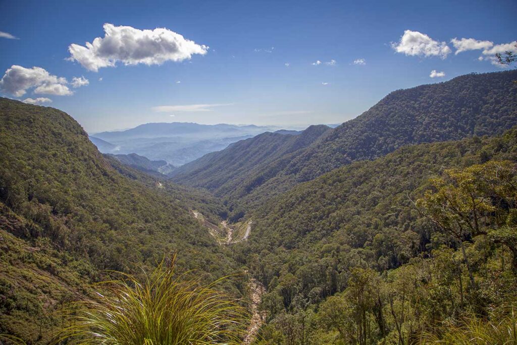 Wide valley view from Khanh Le Pass with layered mountains, forested hills, and a winding road descending toward the lowlands