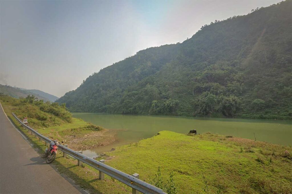 Scenic landscape in Sin Ho district with a river valley, forested hills, and a motorbike parked along a mountain road