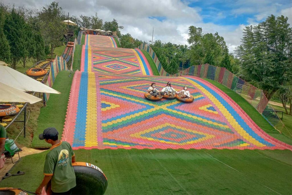 Visitors sliding down the rainbow slide at Mongo Land Dalat on inflatable tubes in a group
