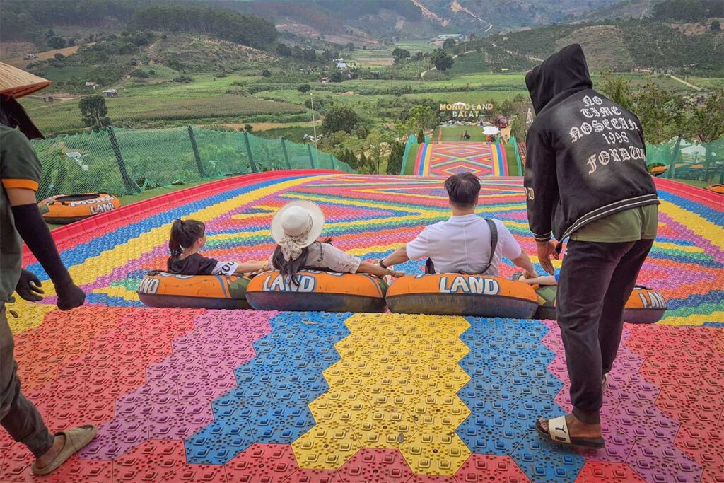 People starting their ride on the rainbow slide at Mongo Land Dalat with staff assisting at the top