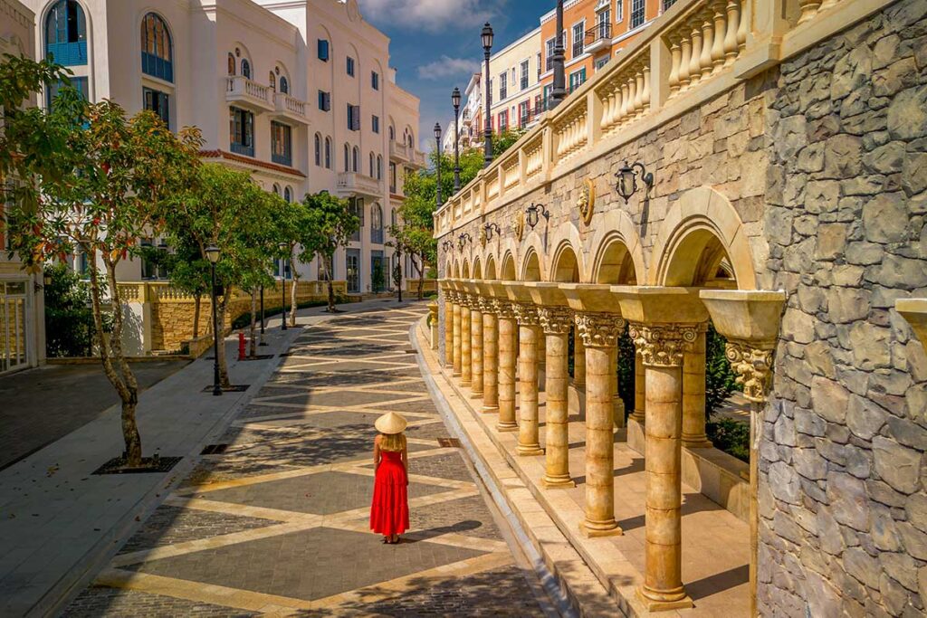 Quiet street in Sunset Town Phu Quoc with European style architecture columns and woman walking in red dress