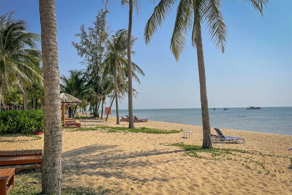 Sun loungers under palm trees on sandy beach at Ong Lang Beach Phu Quoc with calm sea