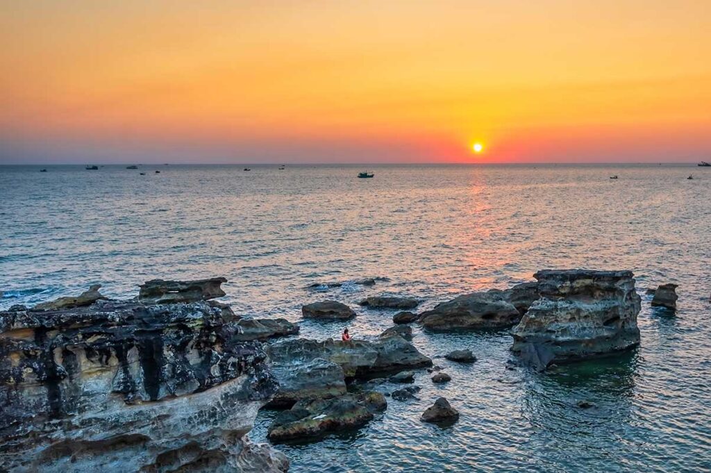 Sunset view near Dinh Cau Temple in Duong Dong Phu Quoc with rocky coastline and sea boats