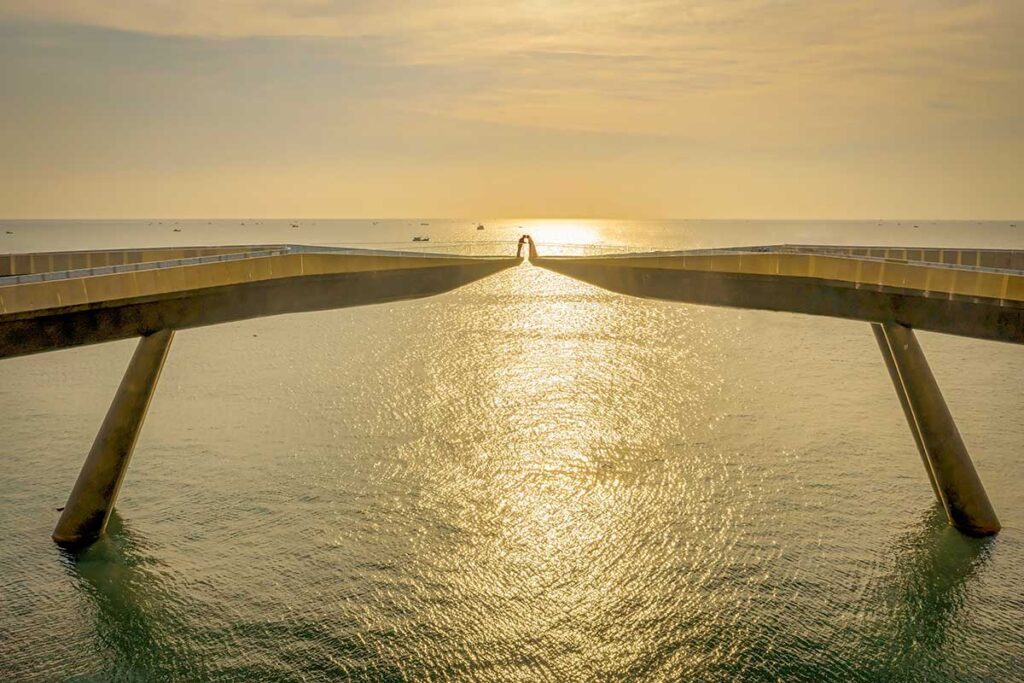 Couple standing at the center of Kiss Bridge Phu Quoc during golden sunset with sunlight reflecting on the sea