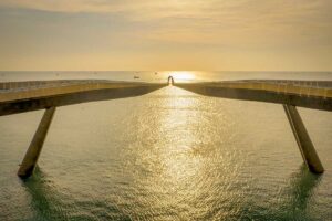 Couple standing at the center of Kiss Bridge Phu Quoc during golden sunset with sunlight reflecting on the sea