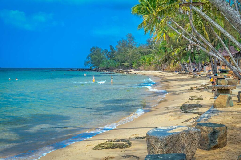 People swimming at sandy shoreline of Ong Lang Beach Phu Quoc with palm trees and calm sea