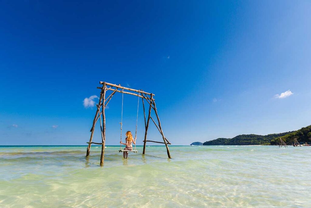 Female traveler on sea swing at Sao Beach Phu Quoc with shallow turquoise water and tropical coast