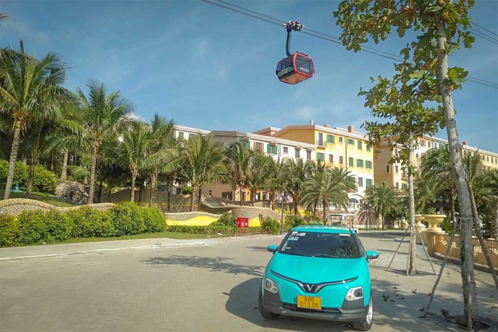Green SM taxi in Phu Quoc parked near Sunset Town with cable car above on sunny day