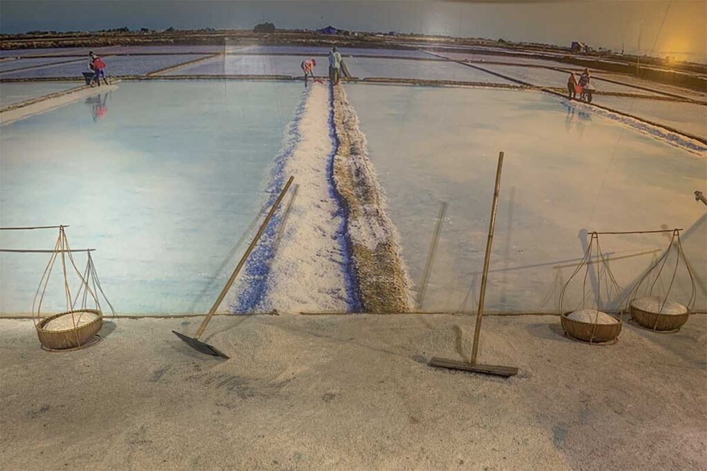 Interactive salt field exhibit at Lang Chai Xua Fish Sauce Museum with real salt, traditional harvesting tools and a panoramic backdrop of salt workers in Phan Thiet