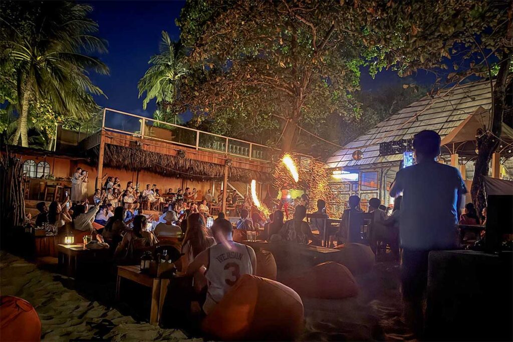 Nighttime fire performance at Aloha Beach Bar in Phu Quoc with beach seating, tropical atmosphere, and crowds watching the show