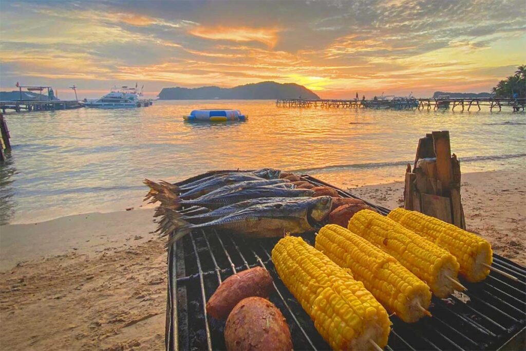 Beach BBQ during a Phu Quoc island hopping tour with grilled seafood and corn at sunset by the sea