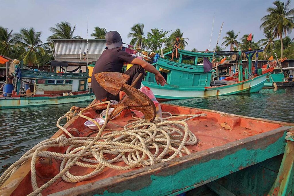 Local fisherman sitting on a wooden boat in Rach Tram Fishing Village Phu Quoc with traditional fishing boats nearby