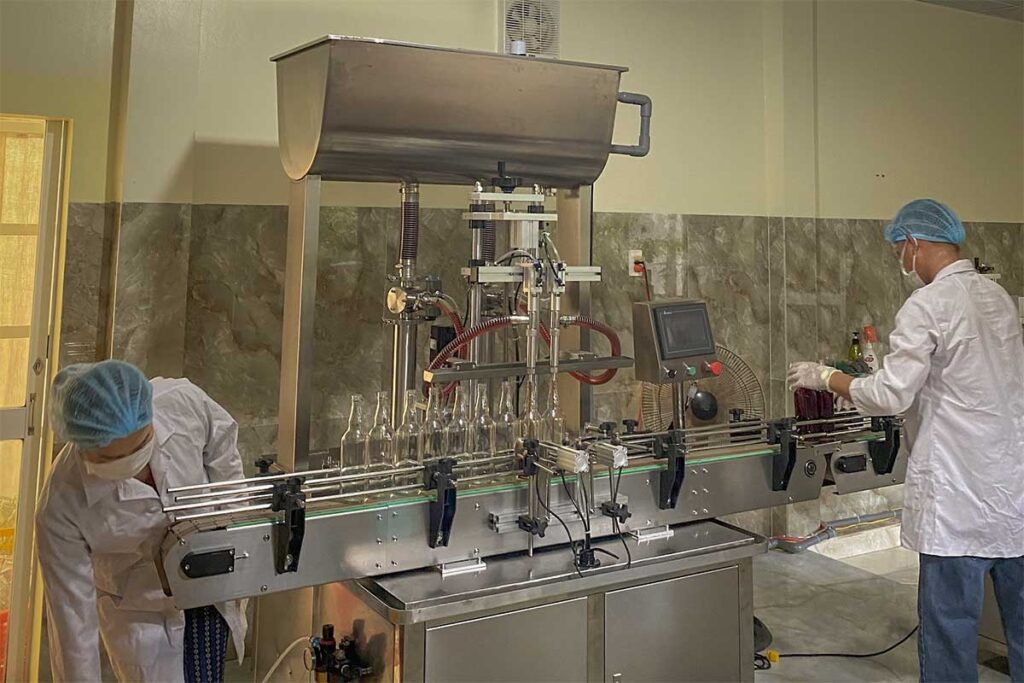 Workers bottling traditional fish sauce at a production facility in Phu Quoc with automated filling machines and glass bottles