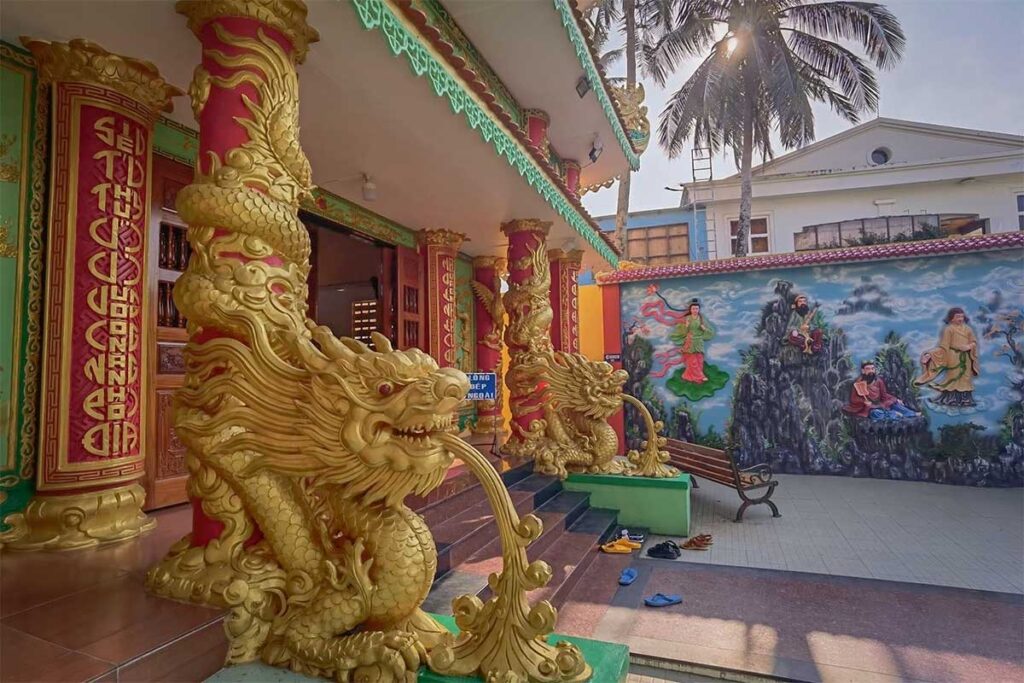 Golden dragon sculptures at the entrance of Dinh Ba Thuy Long Thanh Mau Temple in Phu Quoc with colorful columns and painted wall mural in the courtyard