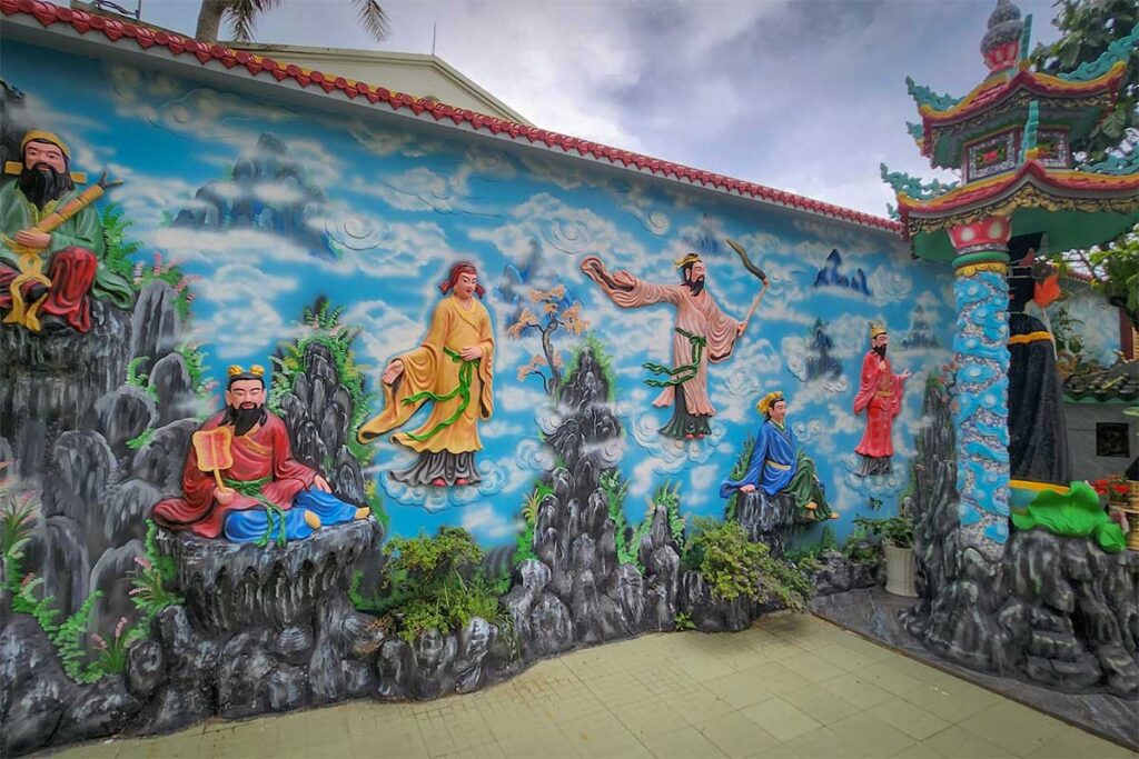 Colorful wall mural at Dinh Ba Thuy Long Thanh Mau Temple in Phu Quoc showing traditional figures mountains and clouds in a decorative courtyard setting