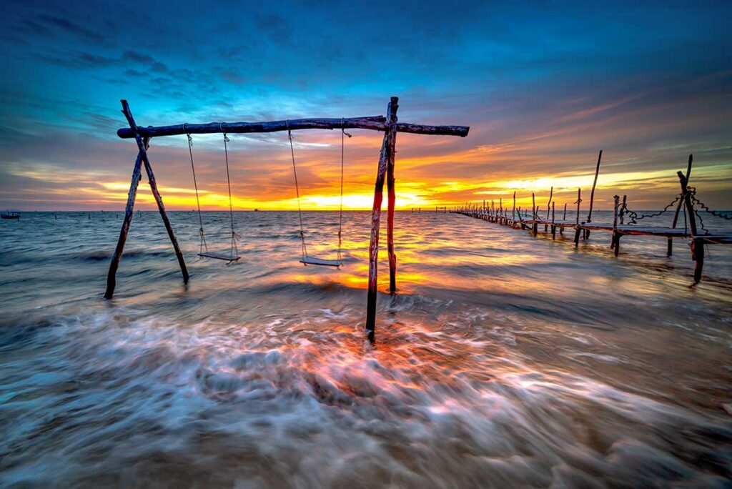 Colorful sunrise over the east coast of Phu Quoc with wooden swings in the sea and waves washing onto the beach