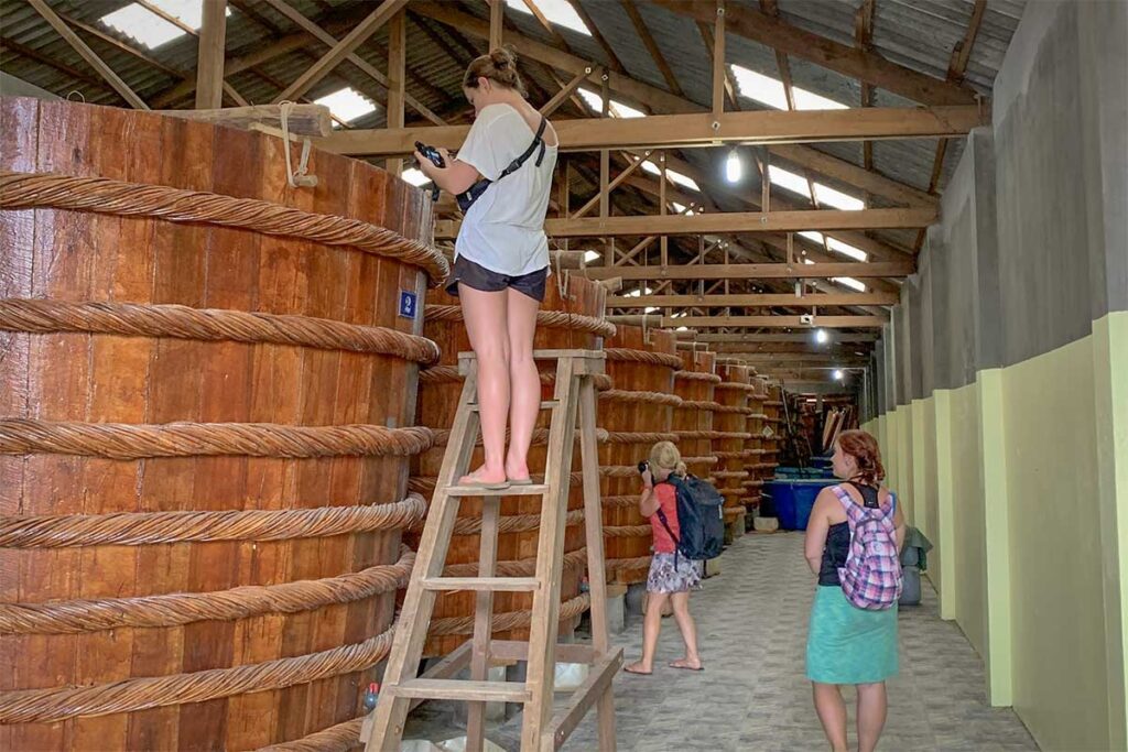 Visitors exploring large wooden fermentation barrels during a fish sauce factory tour in Phu Quoc