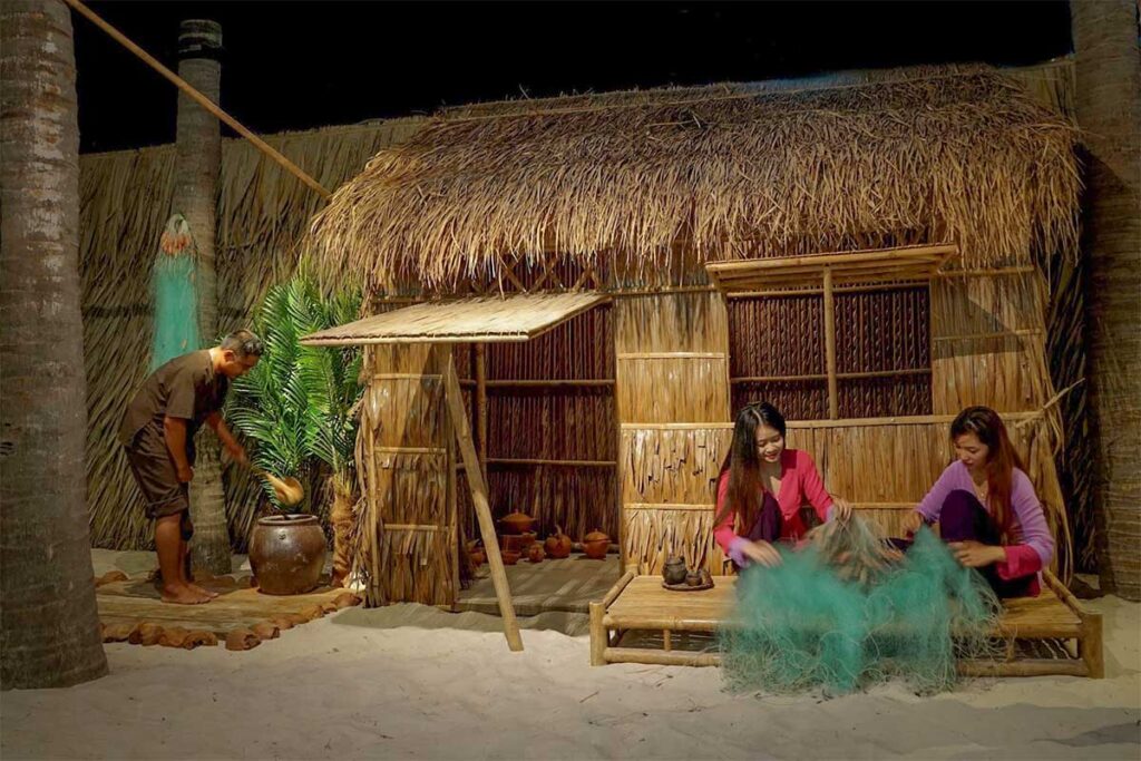 Reconstruction of a traditional Phan Thiet fishing village scene inside Lang Chai Xua Fish Sauce Museum, showing villagers repairing fishing nets beside a thatched hut