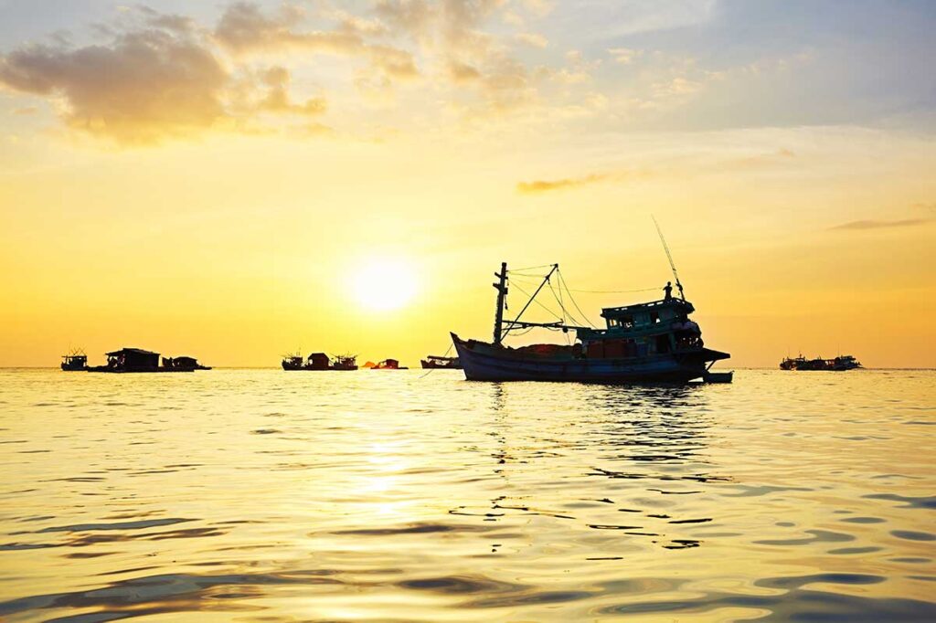 Fishing boats and floating houses during sunrise in Phu Quoc with calm sea water and golden morning light reflecting across the ocean