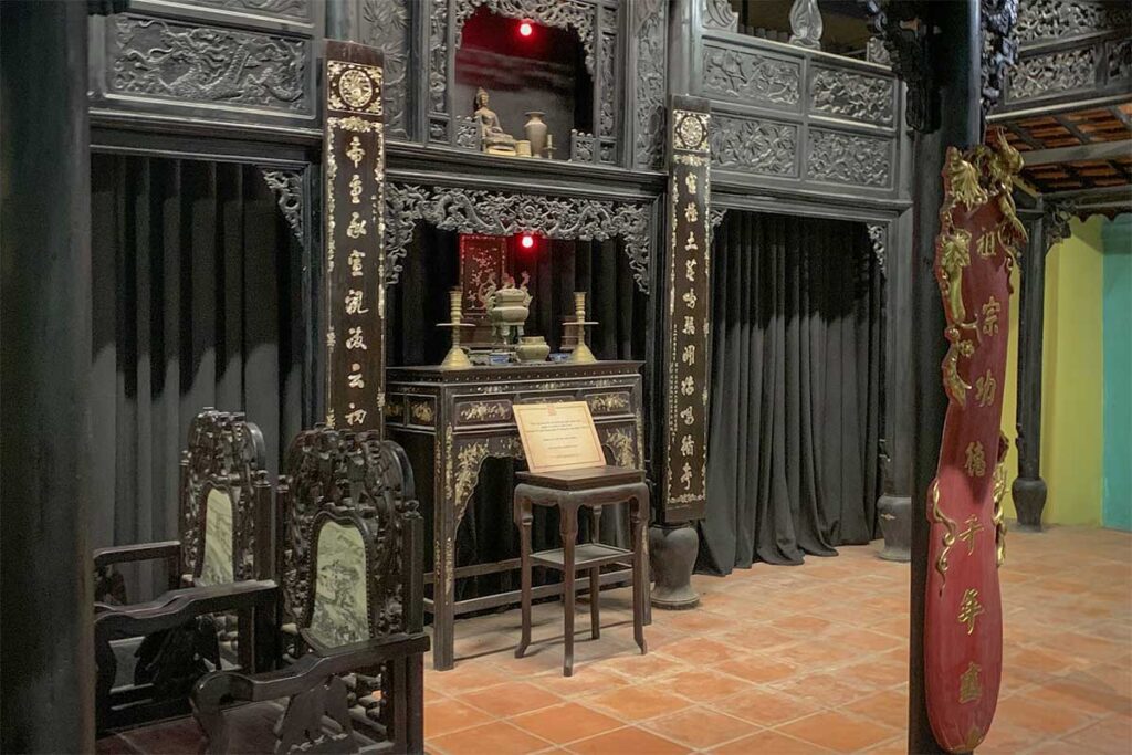 Interior of the Ham Ho ancestral house at Lang Chai Xua Fish Sauce Museum, featuring dark carved wooden furniture, a traditional altar and ornate Vietnamese architecture