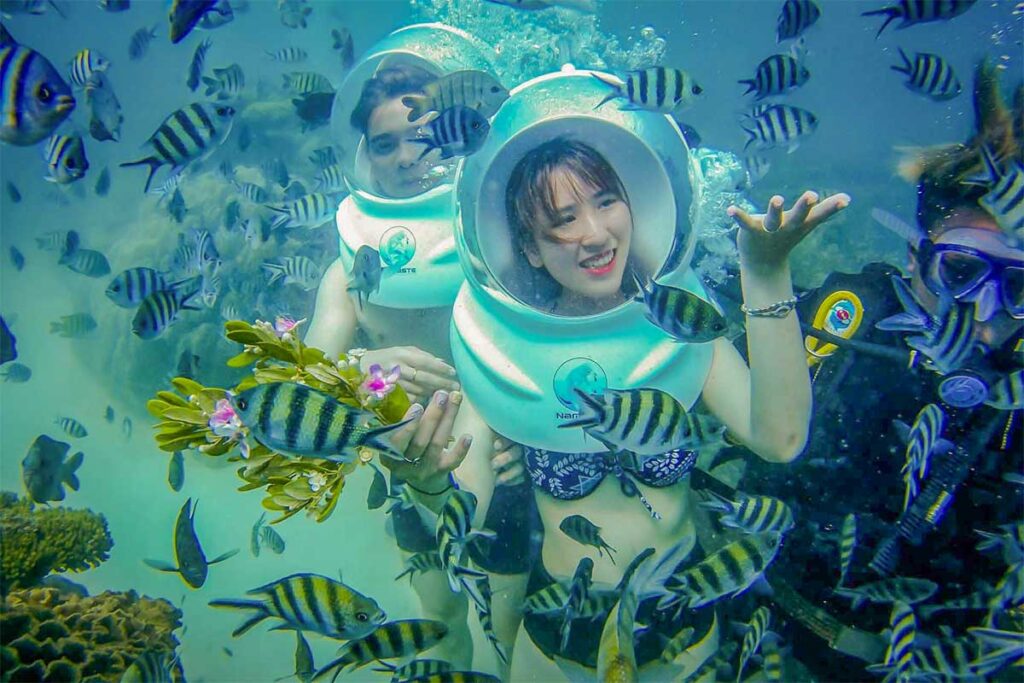 Sea walking tour in Phu Quoc with tourists wearing underwater helmets surrounded by tropical fish and coral reefs