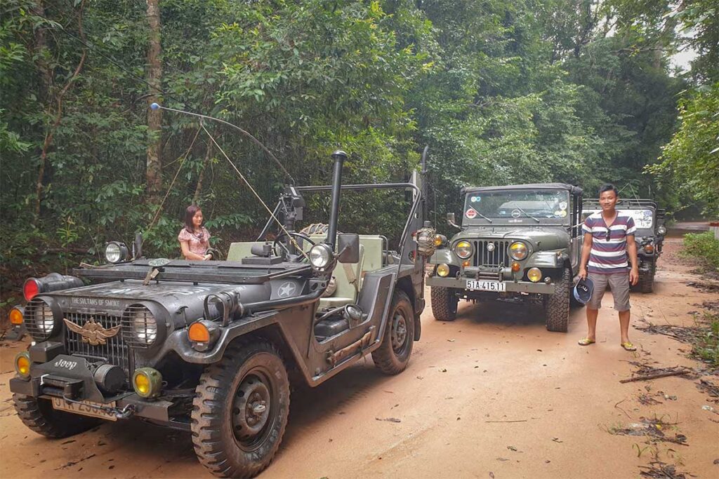 Two vintage military jeeps parked on a red dirt road inside Phu Quoc National Park during an off-road jeep tour through the tropical forest