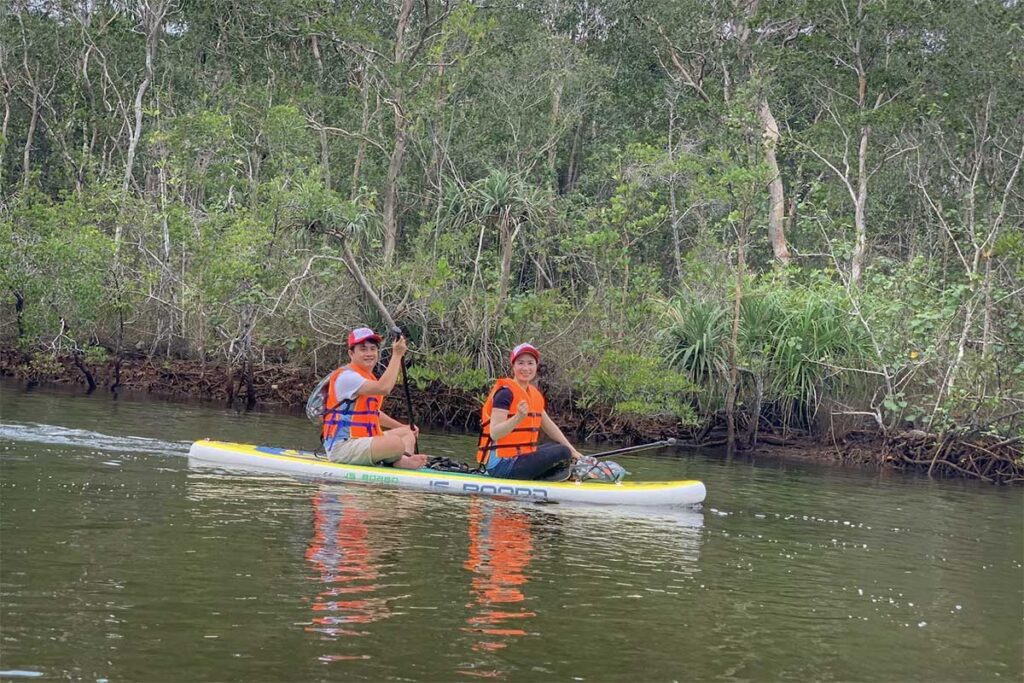 Two travelers kayaking on a calm river lined with mangrove forest near Phu Quoc National Park, wearing life jackets and enjoying a nature tour on the water