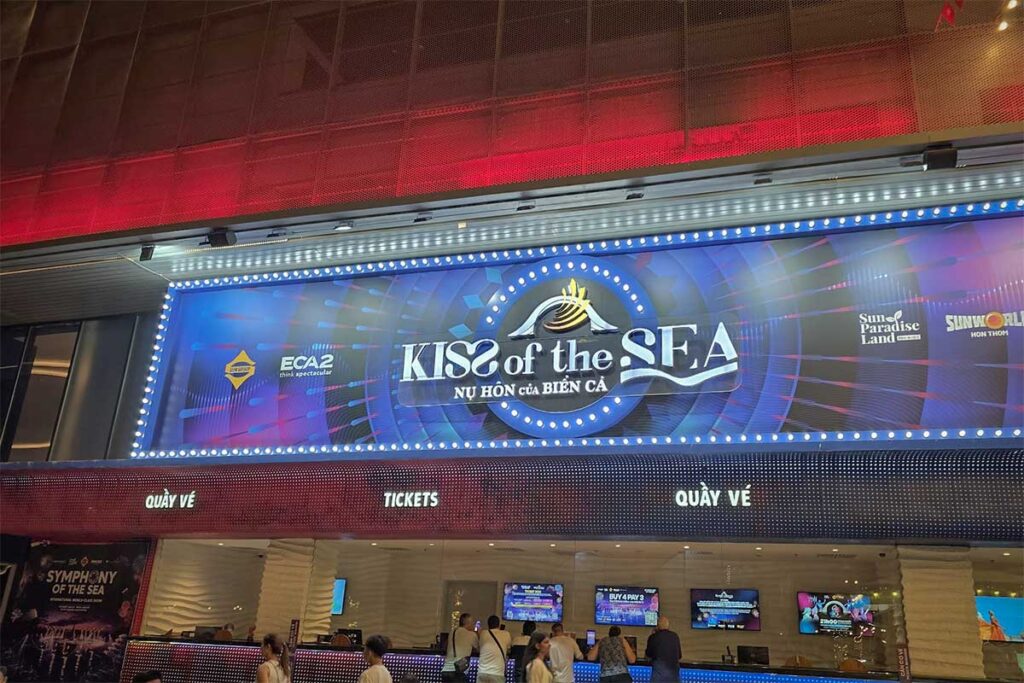 Kiss of the Sea ticket counter in Sunset Town Phu Quoc with illuminated sign above and visitors buying tickets at the booth in the evening