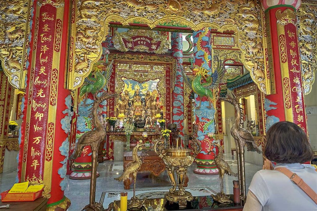 Visitor praying inside Dinh Ba Thuy Long Thanh Mau Temple in Phu Quoc surrounded by ornate pillars incense burner and detailed altar decorations