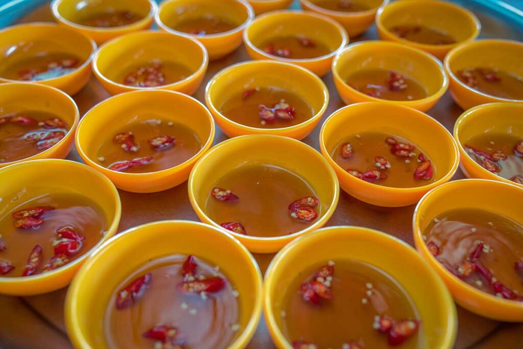Multiple small yellow bowls filled with nuoc cham Vietnamese fish sauce dipping sauce, each garnished with sliced fresh red chili peppers.