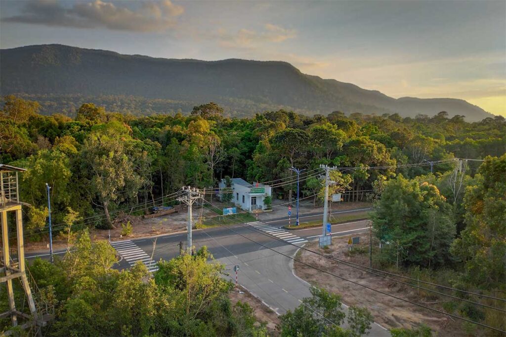 Aerial view of the entrance road to Phu Quoc National Park surrounded by dense tropical forest and the Ham Ninh mountain range in the background