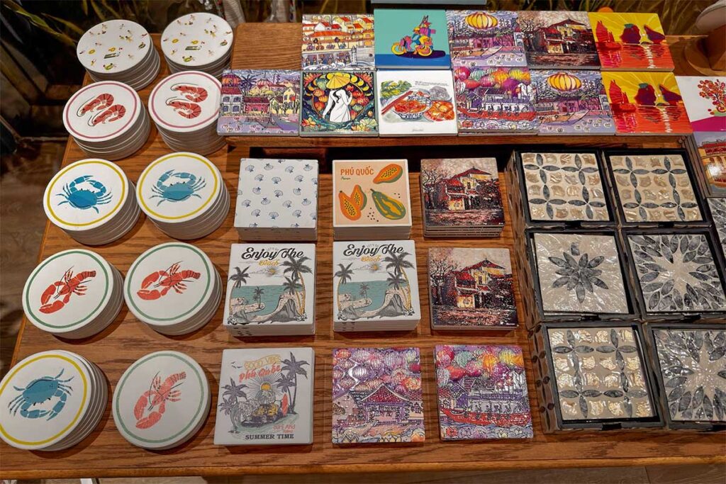 Small souvenir items and decorative coasters for sale in a Phu Quoc gift shop with colorful island artwork shell decorations and beach themed designs