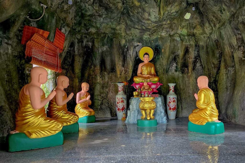 Buddha statue inside cave style shrine at Su Muon Pagoda Phu Quoc with monks kneeling in prayer and natural rock walls