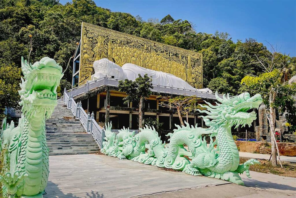 Green dragon staircase at Su Muon Pagoda Phu Quoc leading up to temple with large white reclining Buddha and golden mural in background