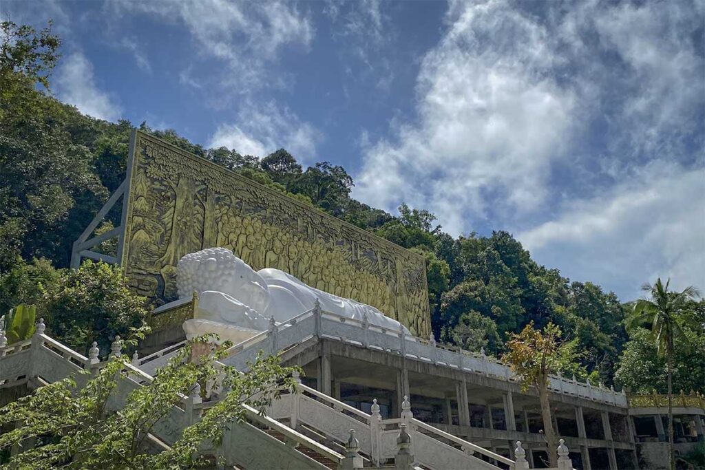 White reclining Buddha statue at Su Muon Pagoda Phu Quoc on elevated platform with stairs and forest hillside backdrop