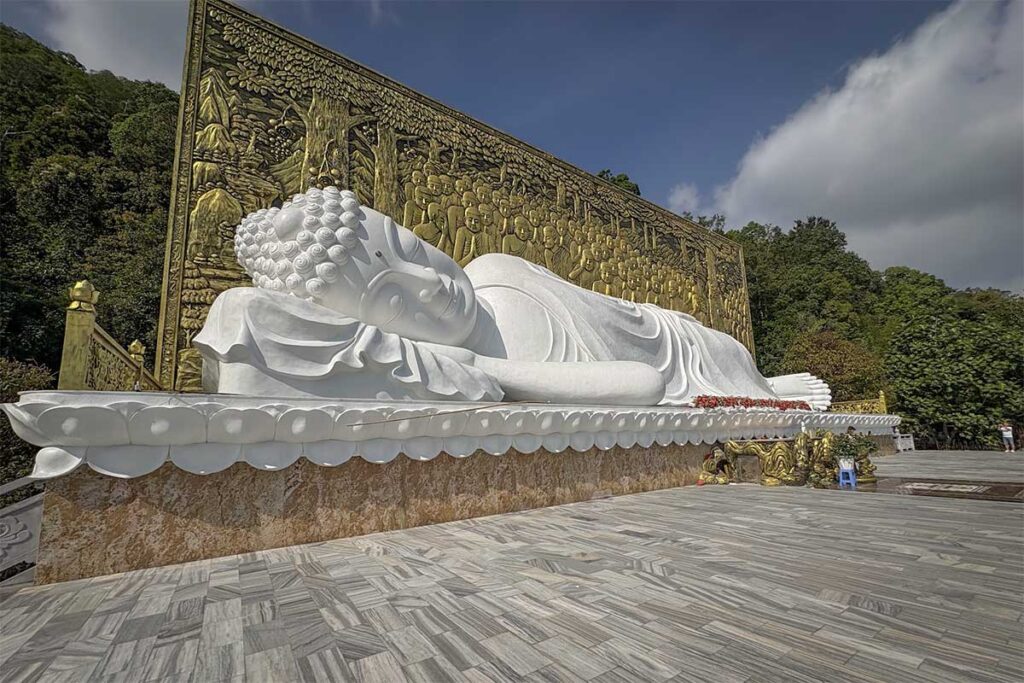 Large white reclining Buddha statue at Su Muon Pagoda Phu Quoc with detailed golden relief wall behind in hillside setting