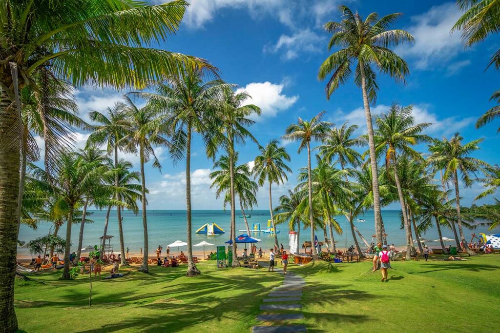 Tourists relaxing at Sun World Hon Thom beach with palm trees grassy area and sea view in Phu Quoc